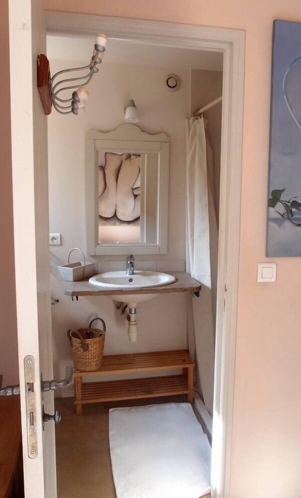 Un baño pequeño con un lavamanos blanco, un espejo de diseño peculiar, una lámpara colgante y una cortina de ducha.