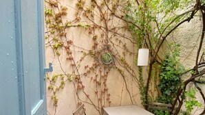 A small outdoor seating area with a table and chairs, surrounded by a wall covered in vines and greenery.
