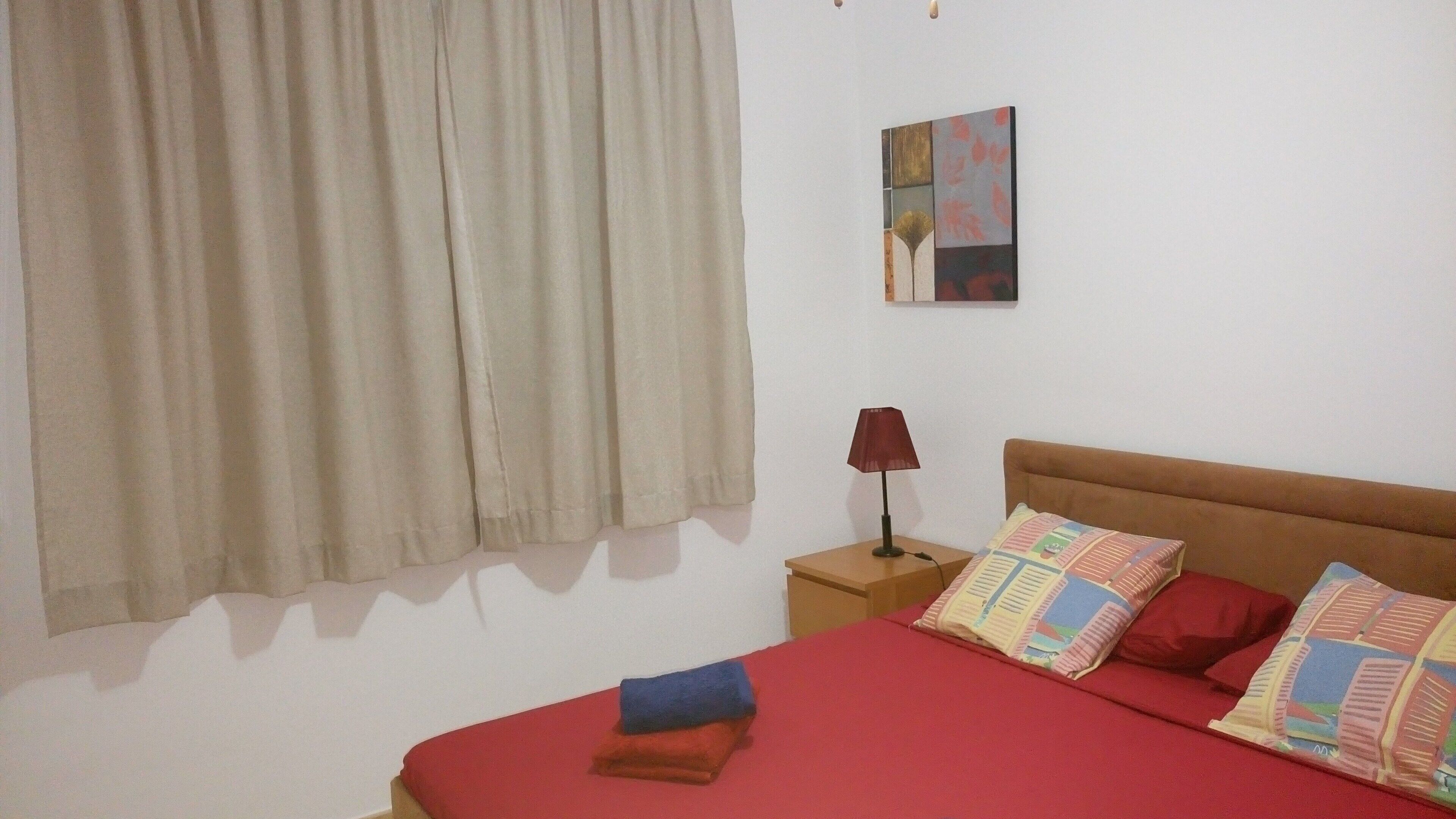 A bedroom with a bed, pillows, a nightstand, a lamp, and a window with curtains.