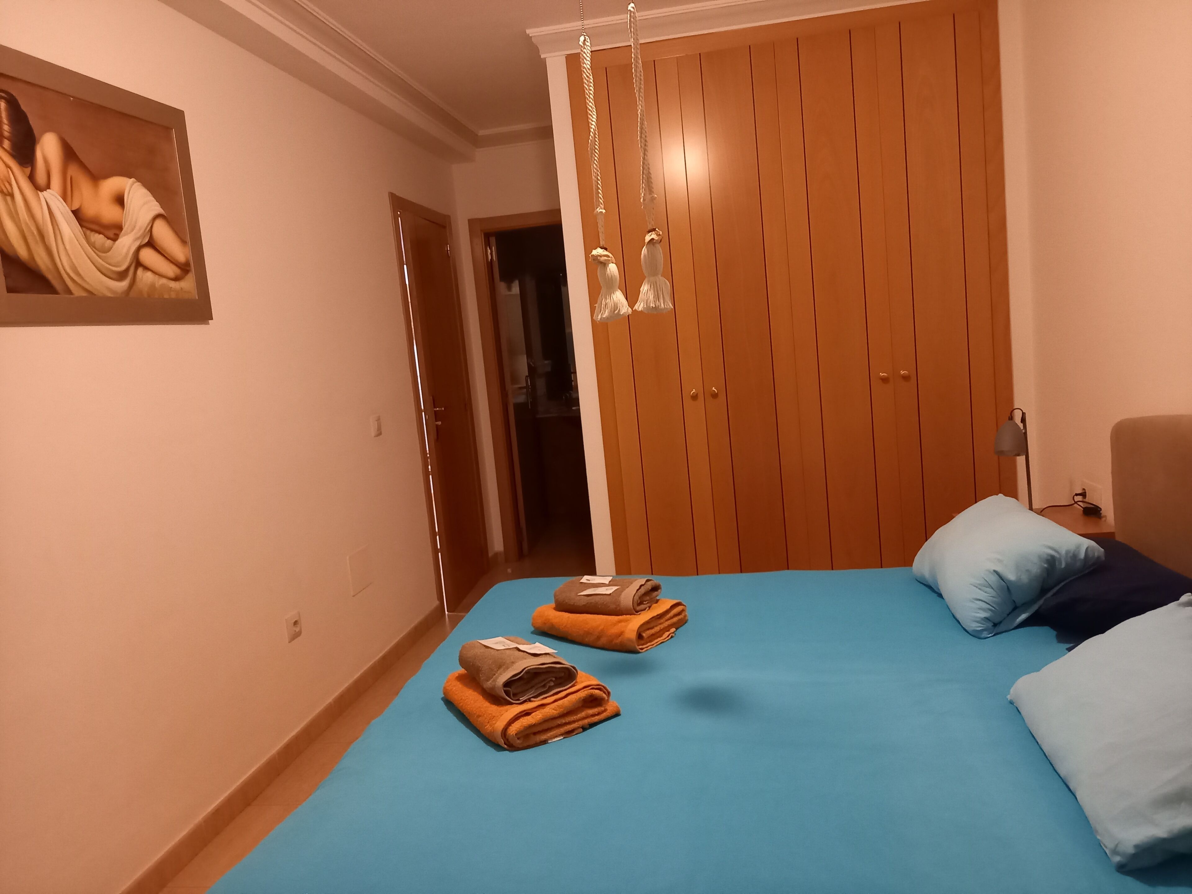 Ein Schlafzimmer mit einem Bett, zwei aufgerollten Handtüchern, einem Gemälde, einem Kleiderschrank und einer Hängeleuchte.