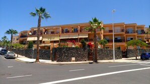 A multi-story hotel with balconies, palm trees, and a stone wall. - SPACIOUS APARTMENT WITH WIFI—large terrace and flower-filled garden, sea and mountain views (Adeje)