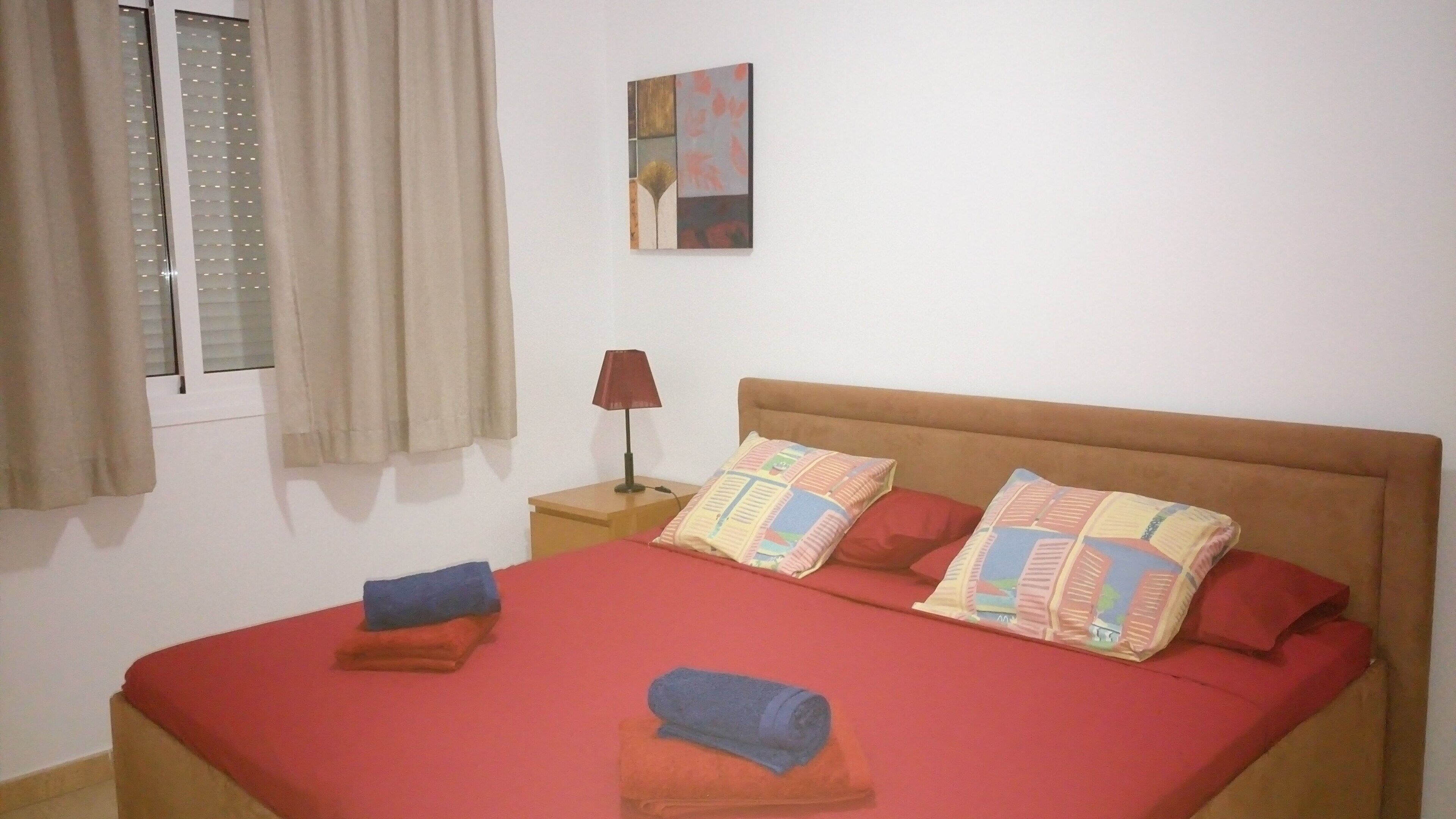 A bedroom with a bed, pillows, a nightstand, a lamp, and a window with curtains.
