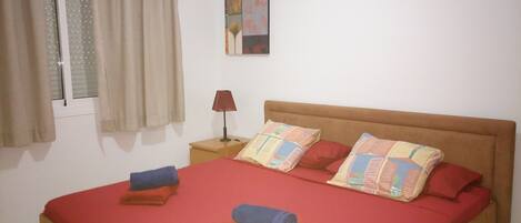 A bedroom with a bed, pillows, a nightstand, a lamp, and a window with curtains.