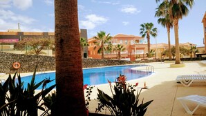 A swimming pool with a stone wall, palm trees, and lounge chairs. - SPACIOUS APARTMENT WITH WIFI—large terrace and flower-filled garden, sea and mountain views (Adeje)