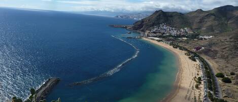 A coastal landscape with a beach, a clear blue sea, and a mountainous backdrop.