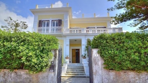 Un edificio de dos pisos con fachada blanca, un balcón en el piso superior y una escalera que conduce a la entrada.