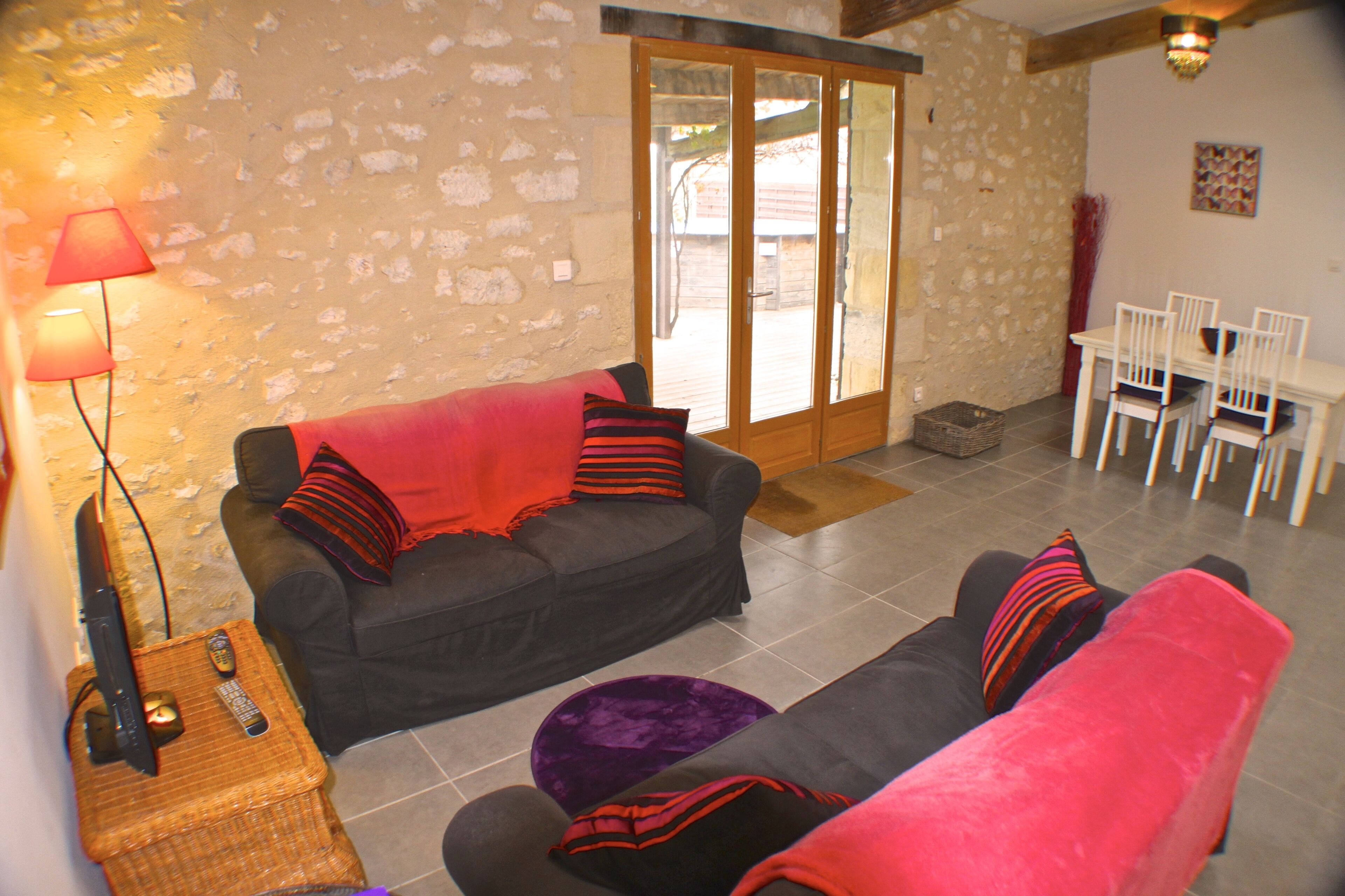 A living room with a sofa, a small table with a lamp, and a dining area with chairs and a table.