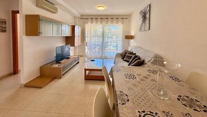 Una sala de estar moderna con sofá, mesa de centro y televisor. Hay una puerta corrediza de vidrio que da a un espacio exterior.