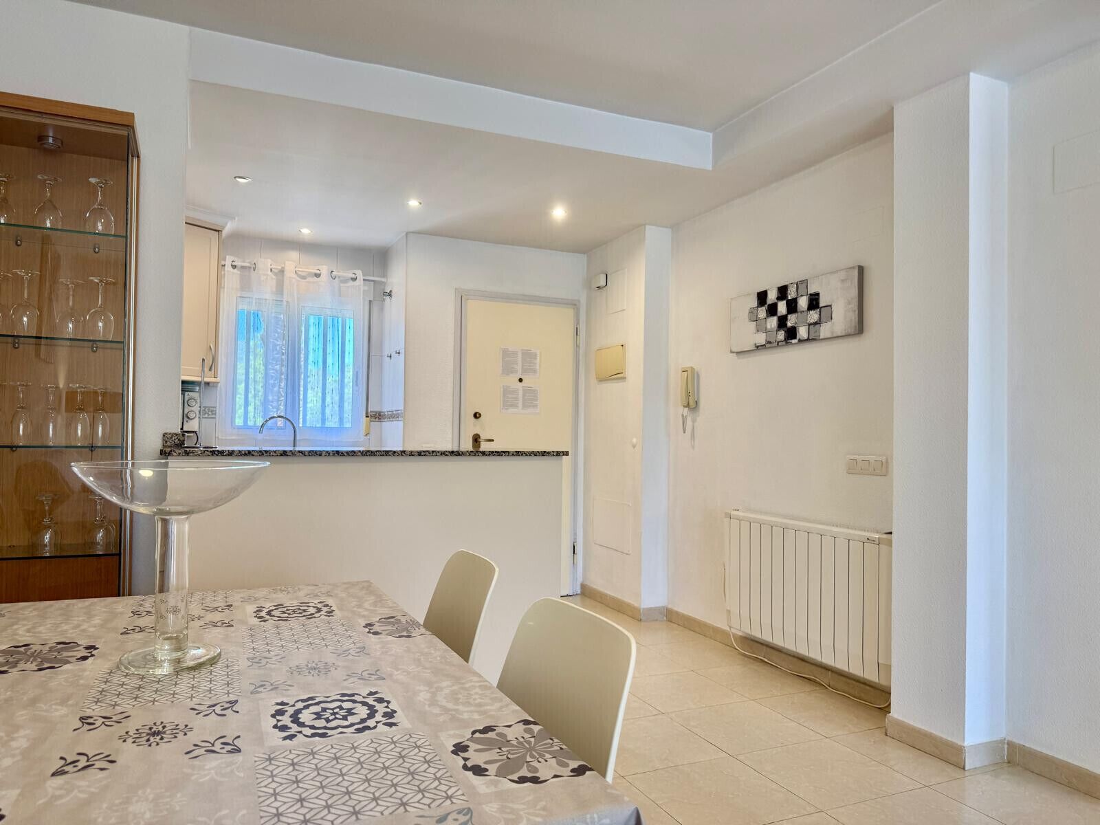 A dining area with a table set for four, a glass-top table, and a cabinet with wine glasses.