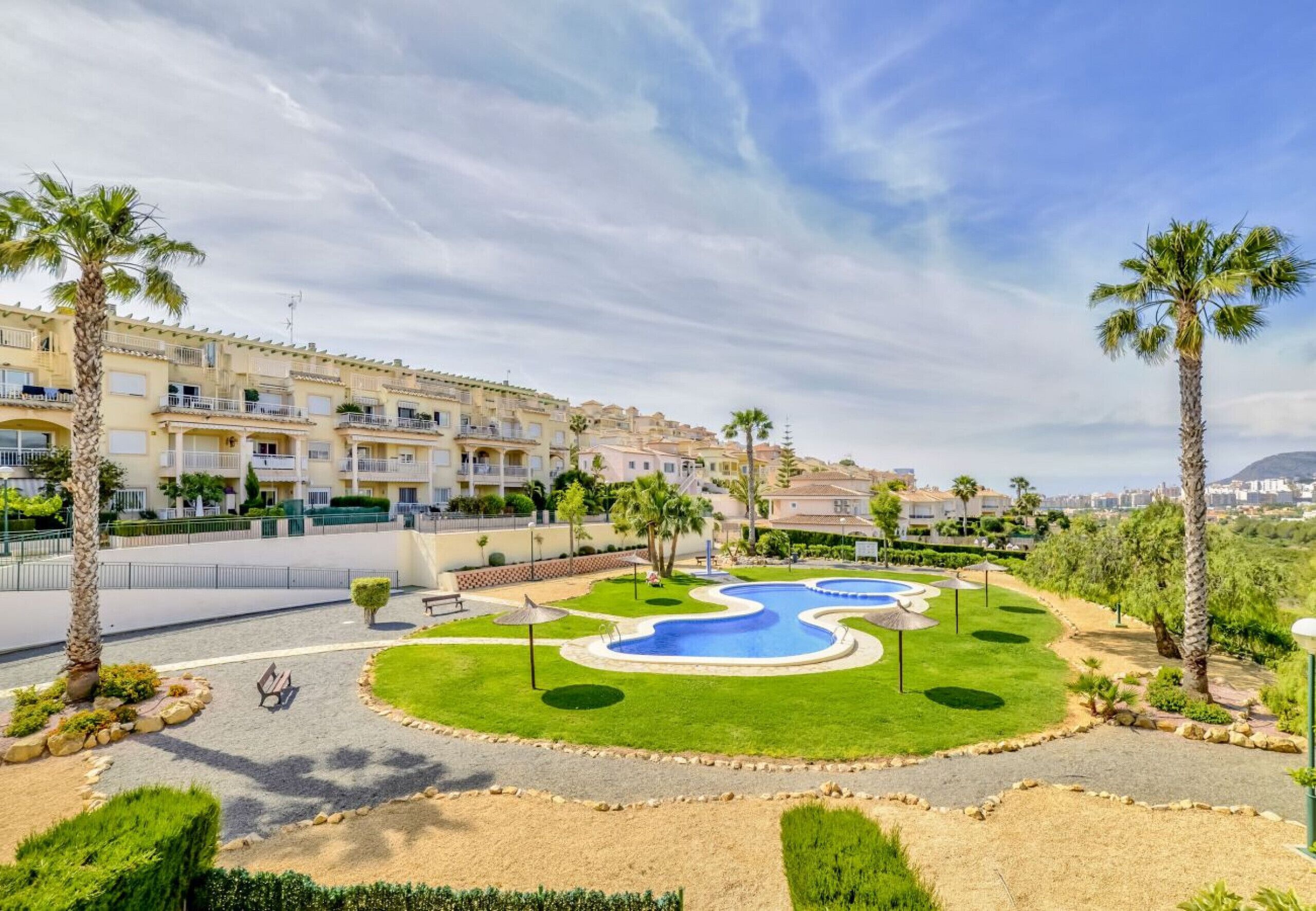 A resort with a swimming pool, palm trees, and a view of a residential area.