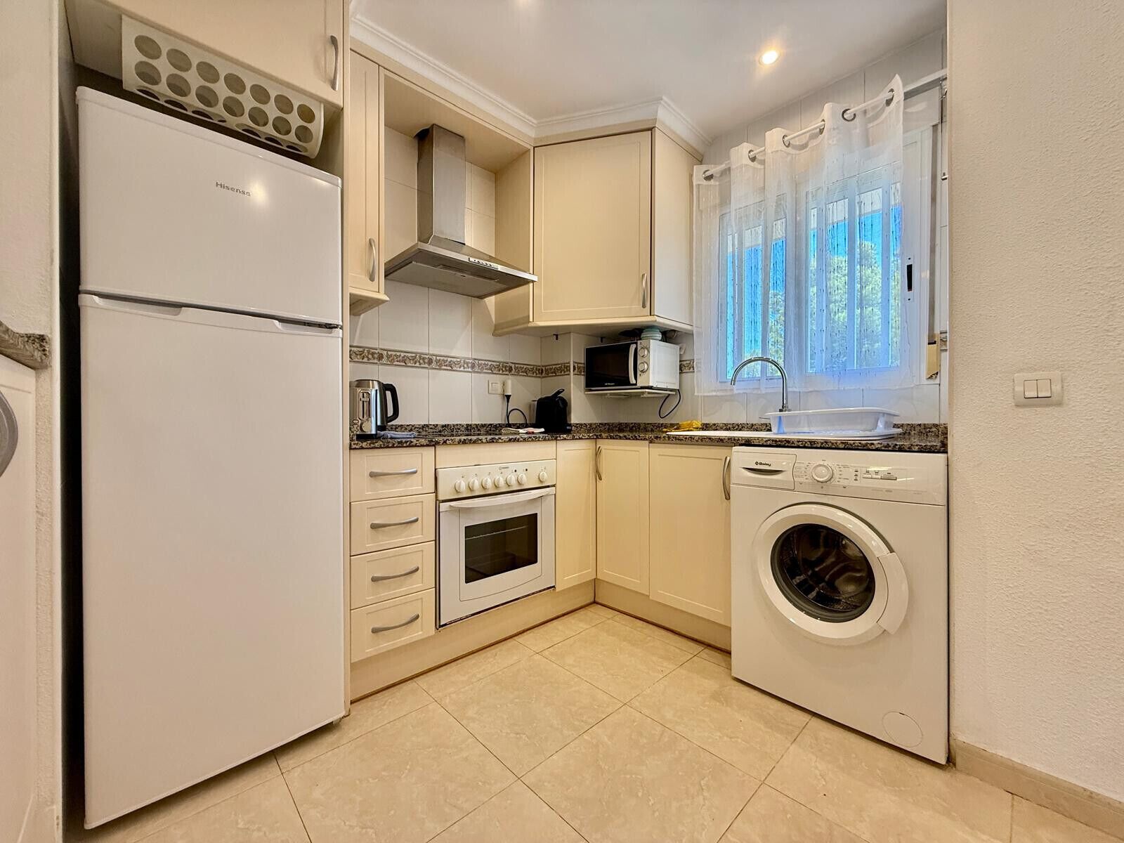 A compact kitchen with a refrigerator, oven, microwave, and washing machine.