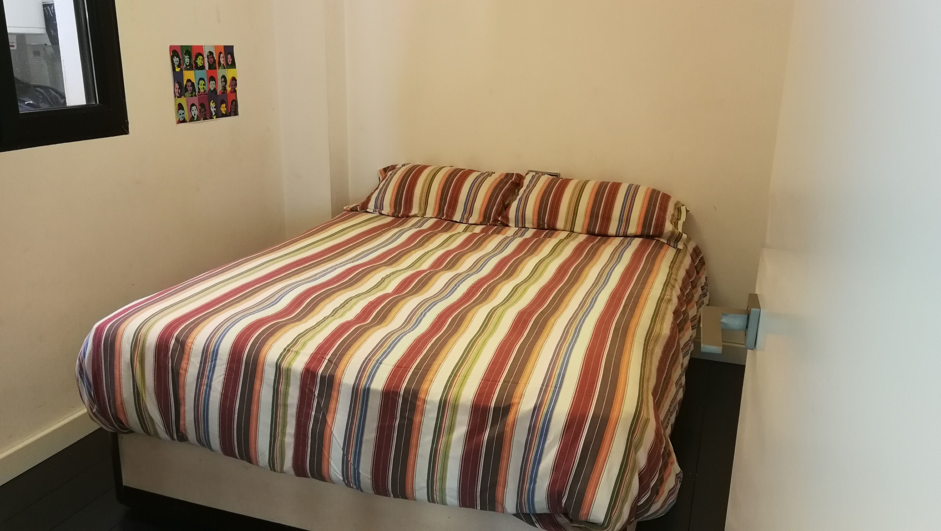 Una cama individual con una colcha a rayas en una habitación con paredes lisas.