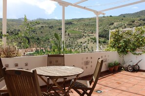 A terrace with a wooden table and chairs, potted plants, and a view of rolling hills. - Apartment with caracter (Pinos Genil)
