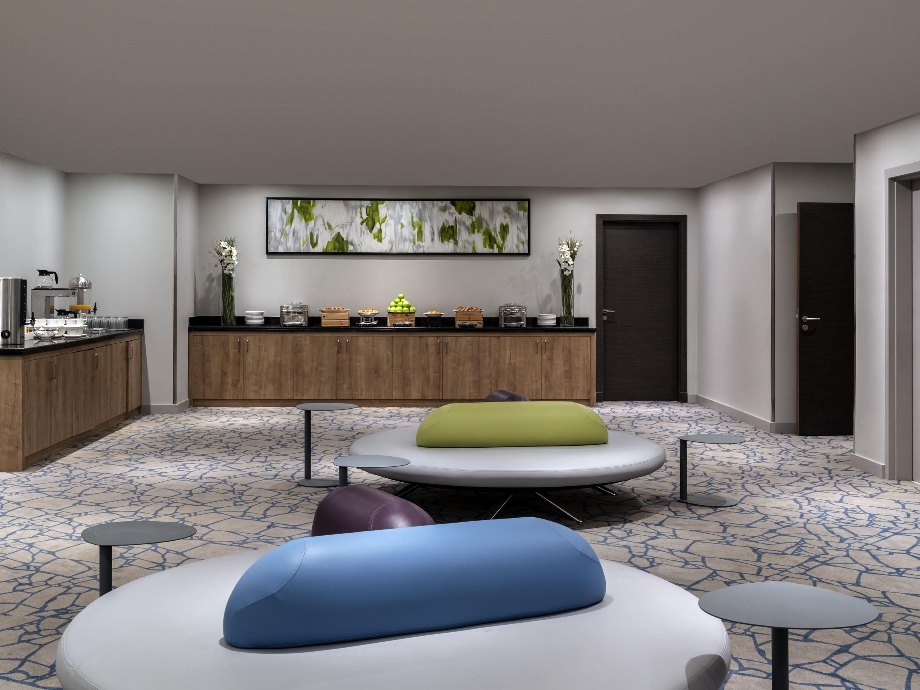 Un vestíbul d'hotel modern amb una zona de seients, una barra de cuina amb menjar i begudes, i una porta.