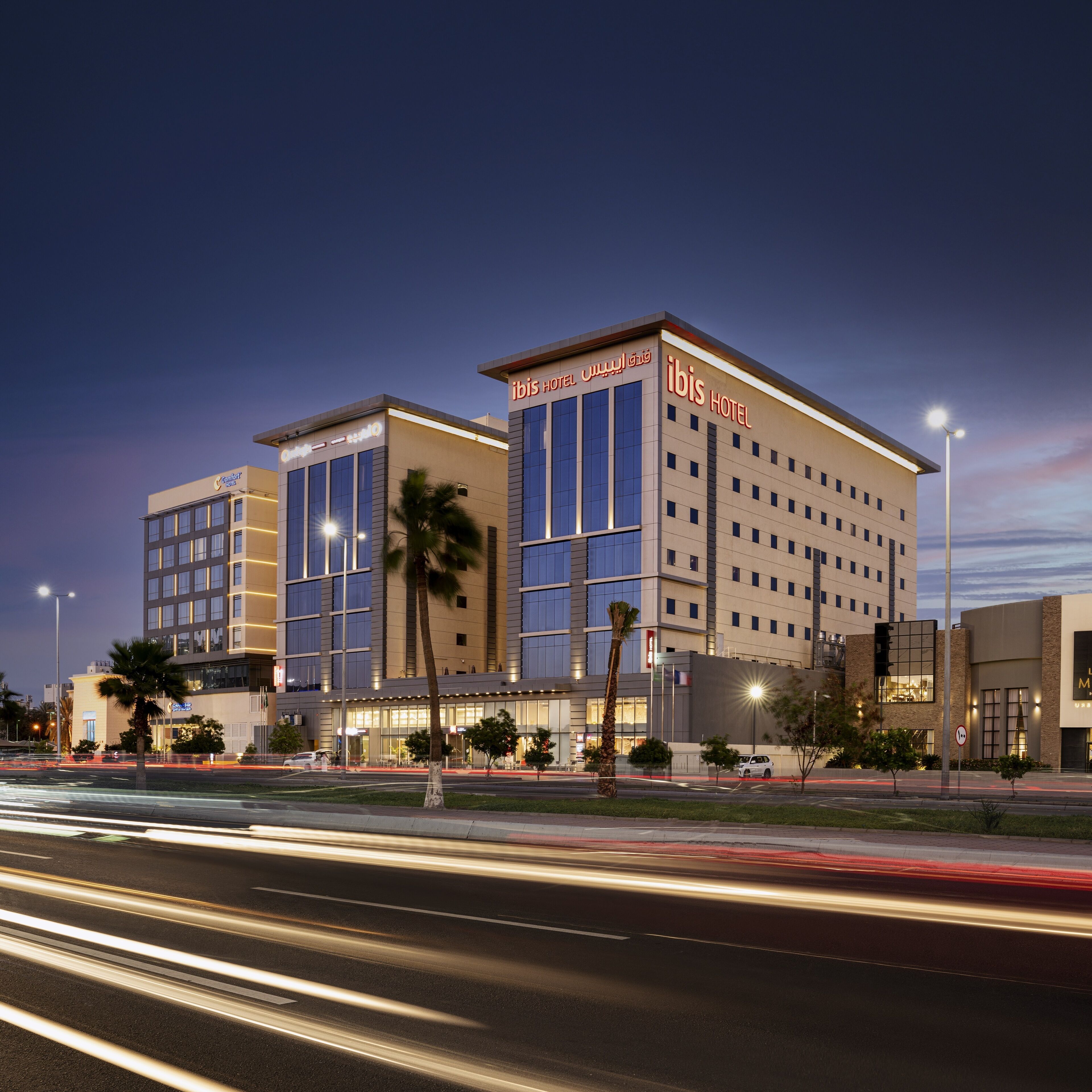 Un hôtel moderne à plusieurs étages, doté de grandes fenêtres et d’une enseigne « ibis hotel » bien visible.
