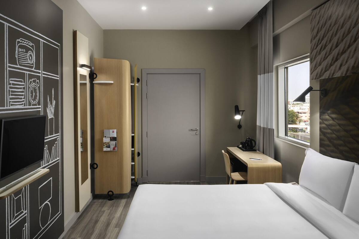A hotel room with a bed, a desk, a TV, and a wardrobe.