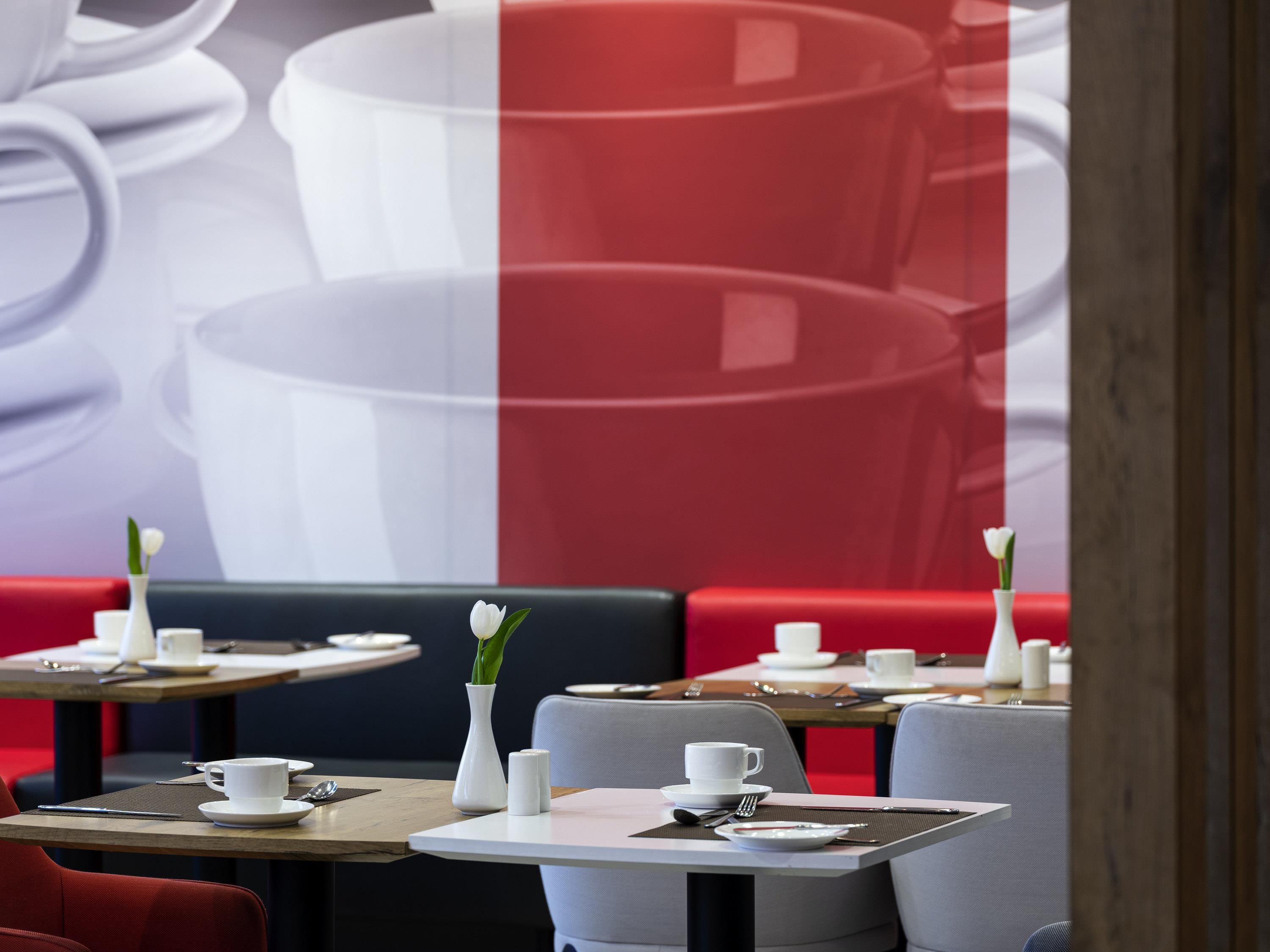 A restaurant with tables set for dining, featuring white cups and saucers, and a vase with a single white flower on each table.
