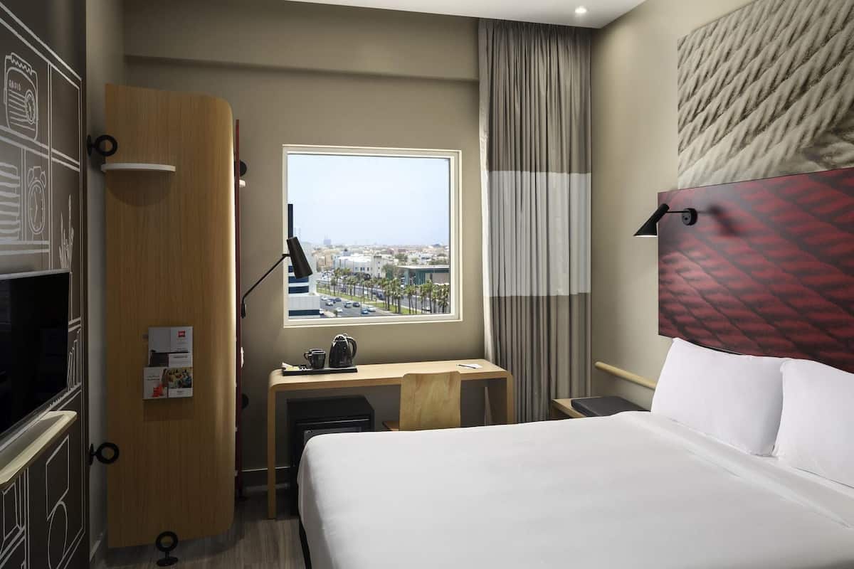 A hotel room with a bed, desk, and a window with a city view.