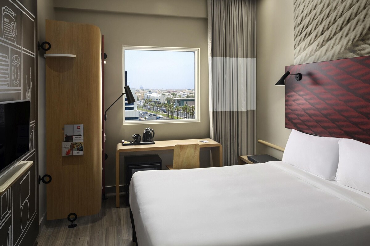 Een hotelkamer met een bed, bureau en een raam met uitzicht op de stad.