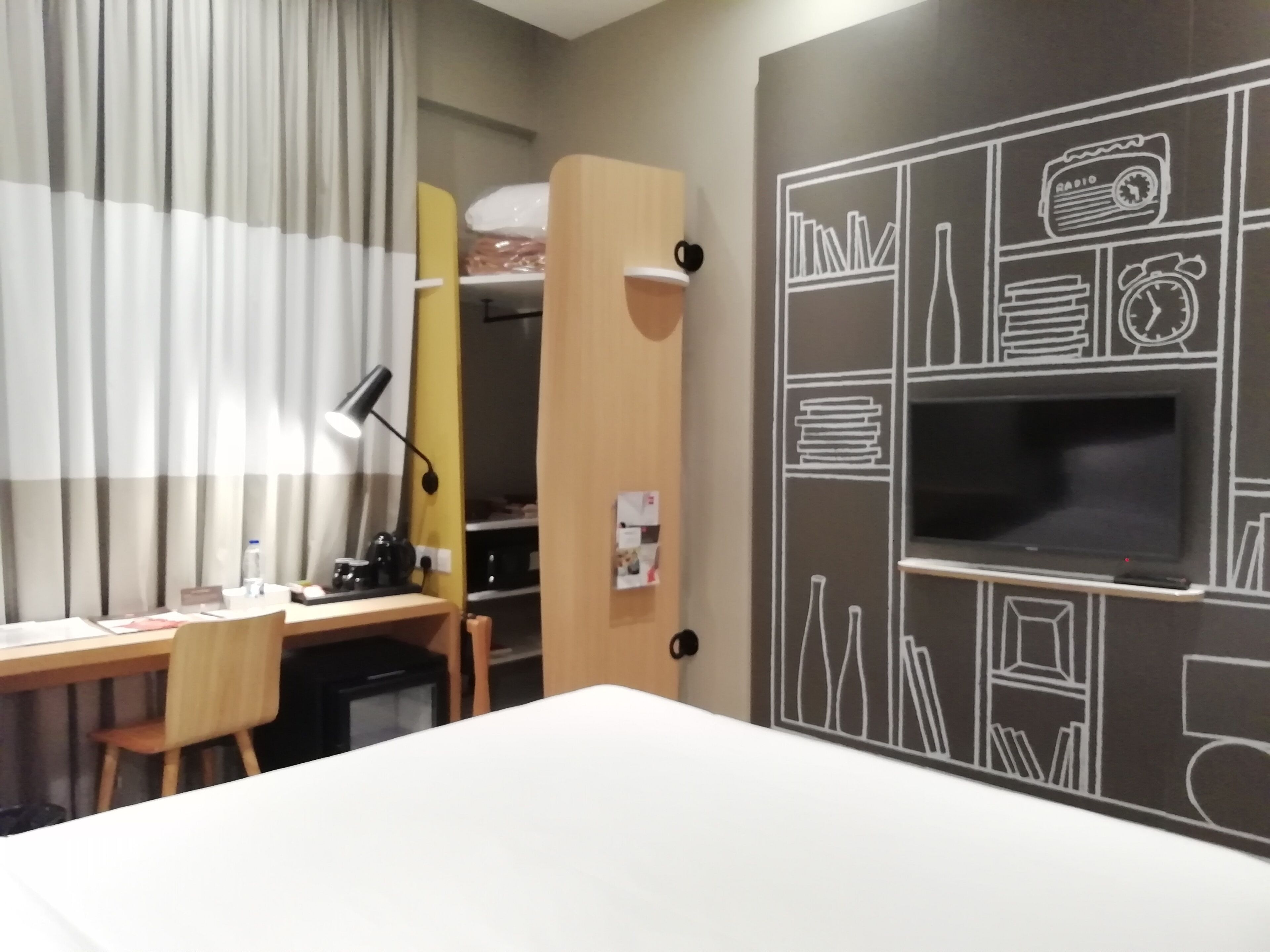 Habitación de hotel con una cama, un escritorio con silla, televisión y armario.
