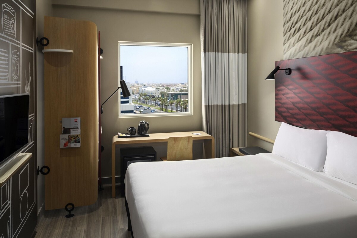 Une chambre d’hôtel avec un lit, un bureau et une fenêtre donnant sur la ville.