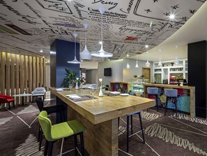 A modern bar area with a wooden counter, bar stools, and a decorative ceiling with handwritten notes. - ibis Jeddah Malik Road (Jeddah)