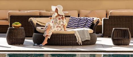 A person relaxing on a wicker sofa with cushions, a striped pillow, and a bowl of fruit beside it.