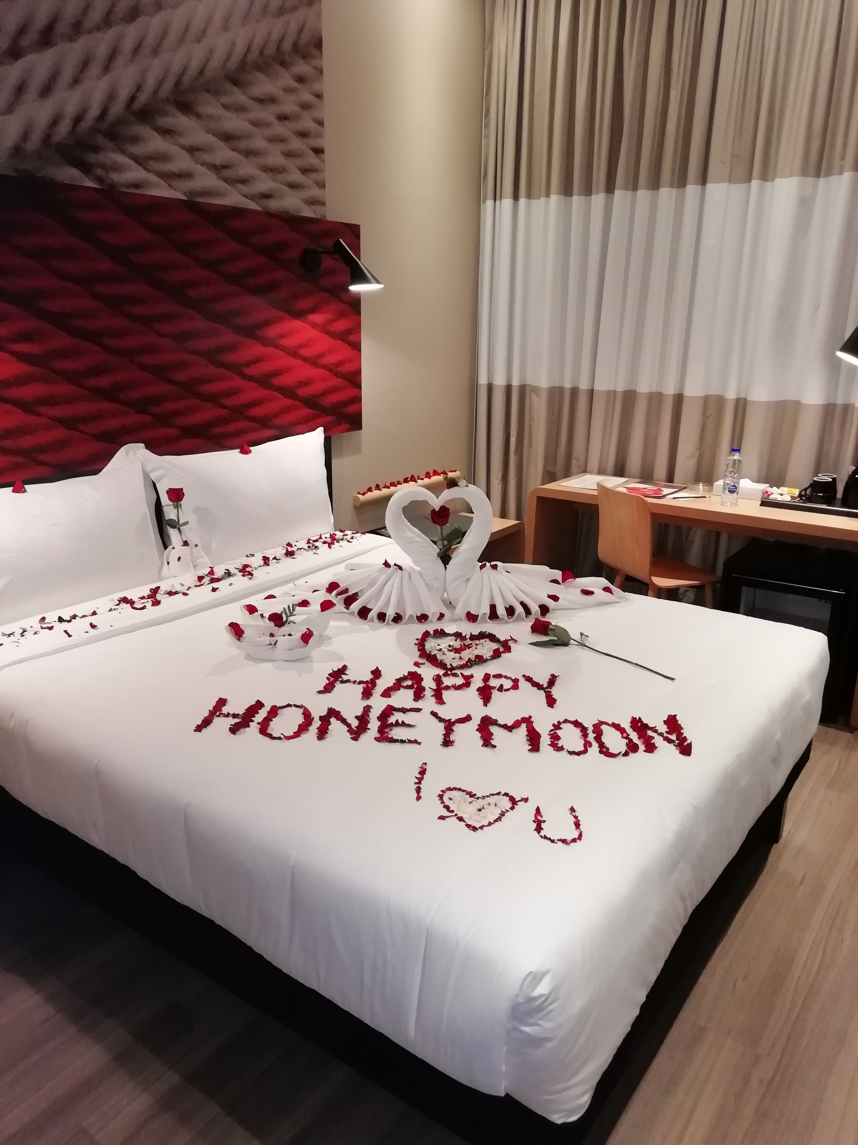 A hotel room with a bed adorned with rose petals and a 'Happy Honeymoon' message.