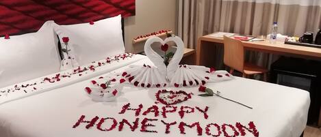 Habitación de hotel con una cama decorada con pétalos de rosa y un mensaje que dice 'Luna de miel feliz'.