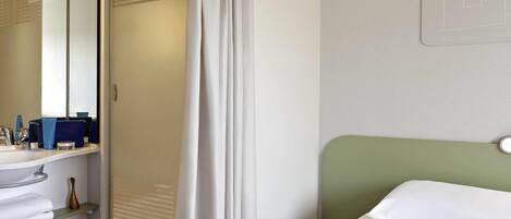 A hotel room with a bed, a nightstand, a mirror, a window with blinds, and a bathroom area with a sink and toiletries.