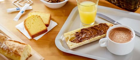 Una bandeja de desayuno con croissants, una rebanada de pan, tostada con crema de chocolate, un vaso de zumo de naranja, una taza de café y un cuenco de granos de café.