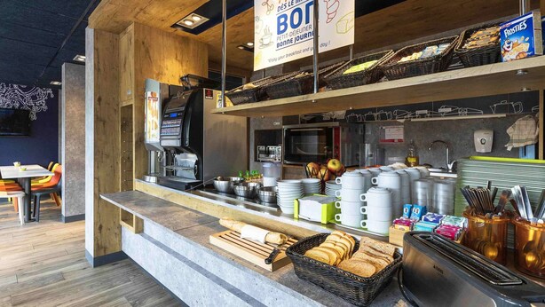 A breakfast bar with a coffee machine, a toaster, and various breakfast items. - ibis budget Saint-Pourçain-sur-Sioule (Saint-Pourcain-sur-Sioule)