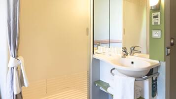 Een badkamer met een douche, wastafel en spiegel.