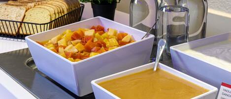 Buffet de café da manhã com frutas, sopa e pão.