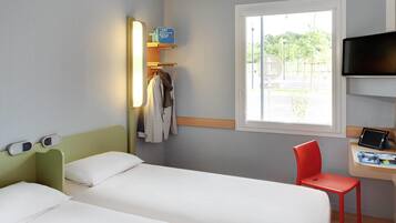 Ein Hotelzimmer mit zwei Betten, einem Schreibtisch mit Stuhl, einem Fernseher und einem Fenster mit Blick auf Grünflächen.
