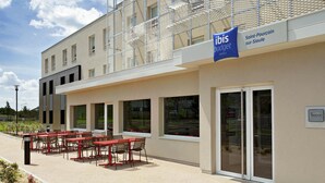 A modern hotel exterior with a covered outdoor seating area and a sign indicating it is an ibis budget hotel. - ibis budget Saint-Pourçain-sur-Sioule (Saint-Pourcain-sur-Sioule)