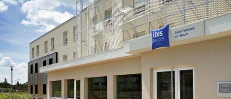A modern hotel exterior with a covered outdoor seating area and a sign indicating it is an ibis budget hotel.