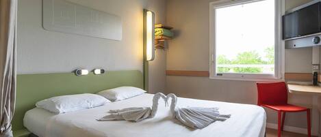 A hotel room with a bed, a desk, a chair, a TV, and a window with a view.