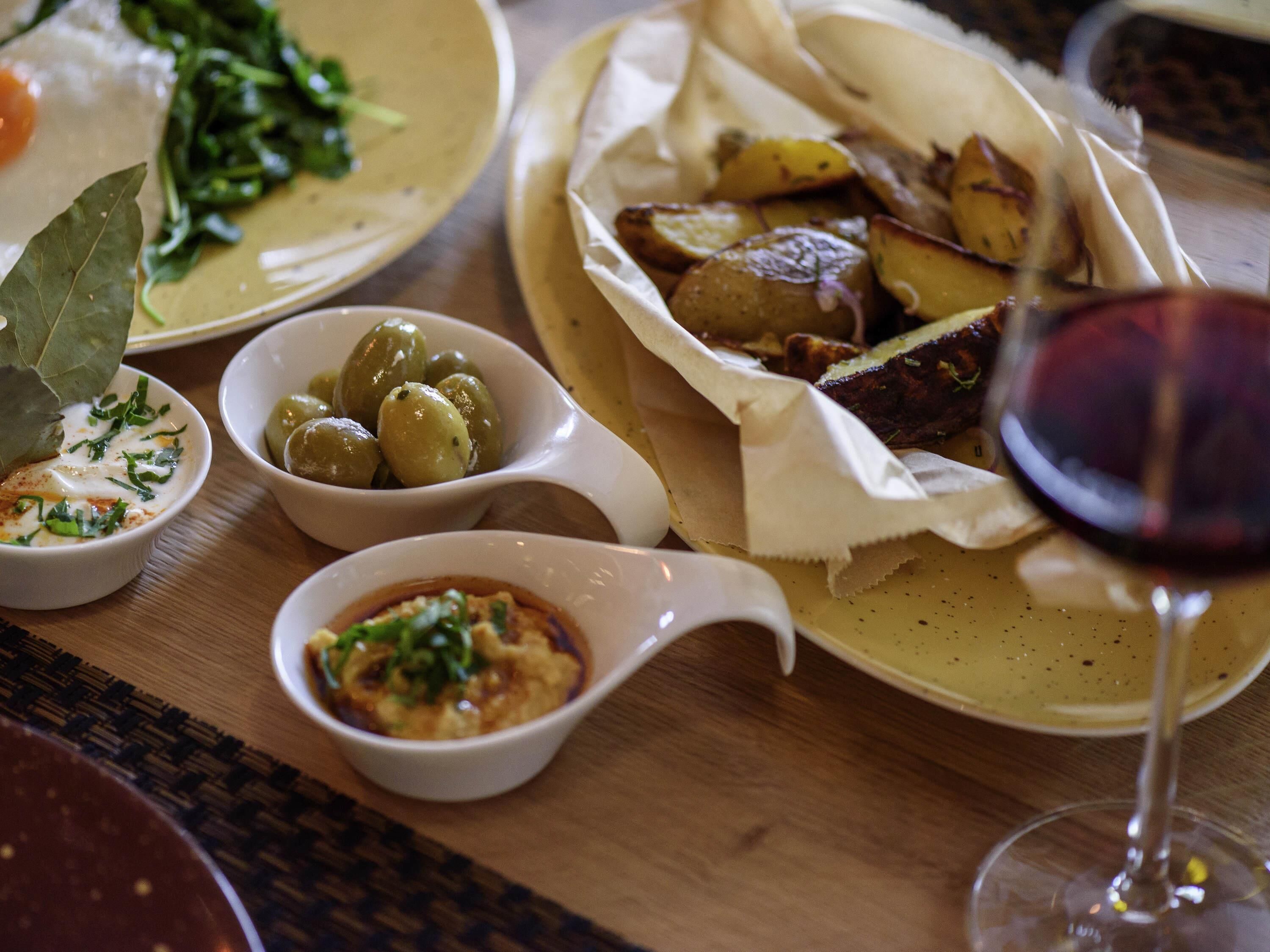 A table with various dishes including olives, a salad, and a glass of red wine.