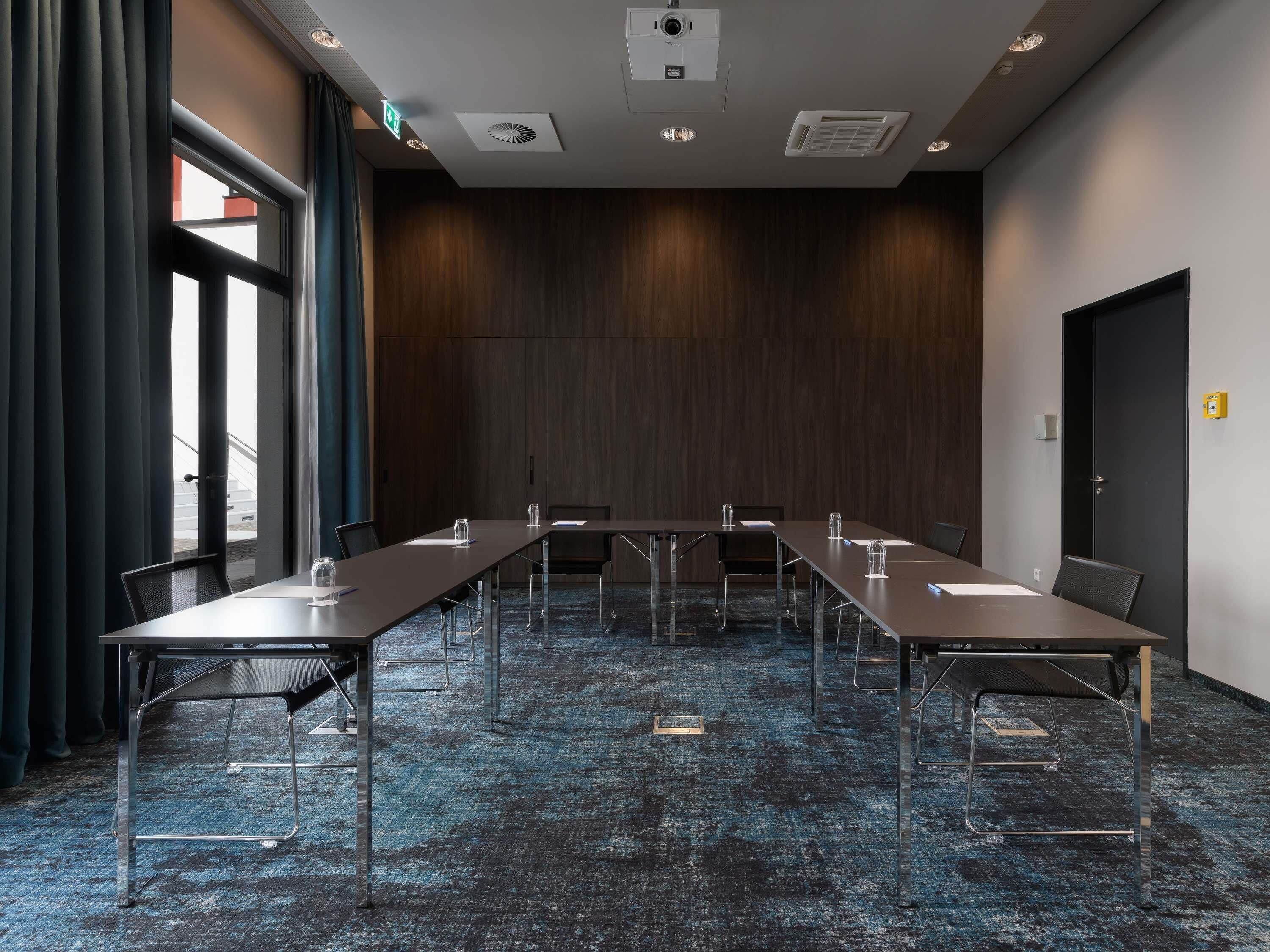 A conference room with a long table, chairs, and a dark wooden wall.