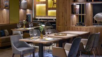 A modern restaurant interior with wooden paneling, tables set with wine glasses, and a bookshelf with books and decorative items.