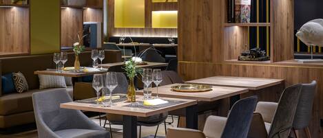 A modern restaurant interior with wooden paneling, tables set with wine glasses, and a bookshelf with books and decorative items.