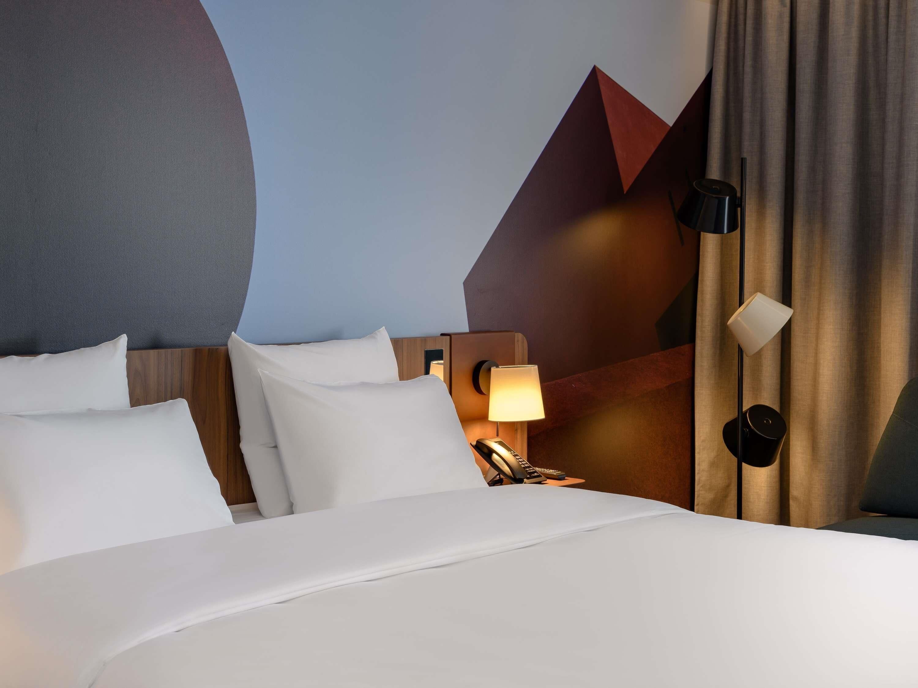 Une chambre d’hôtel avec un lit, une table de chevet avec une lampe et un motif géométrique sur le mur.