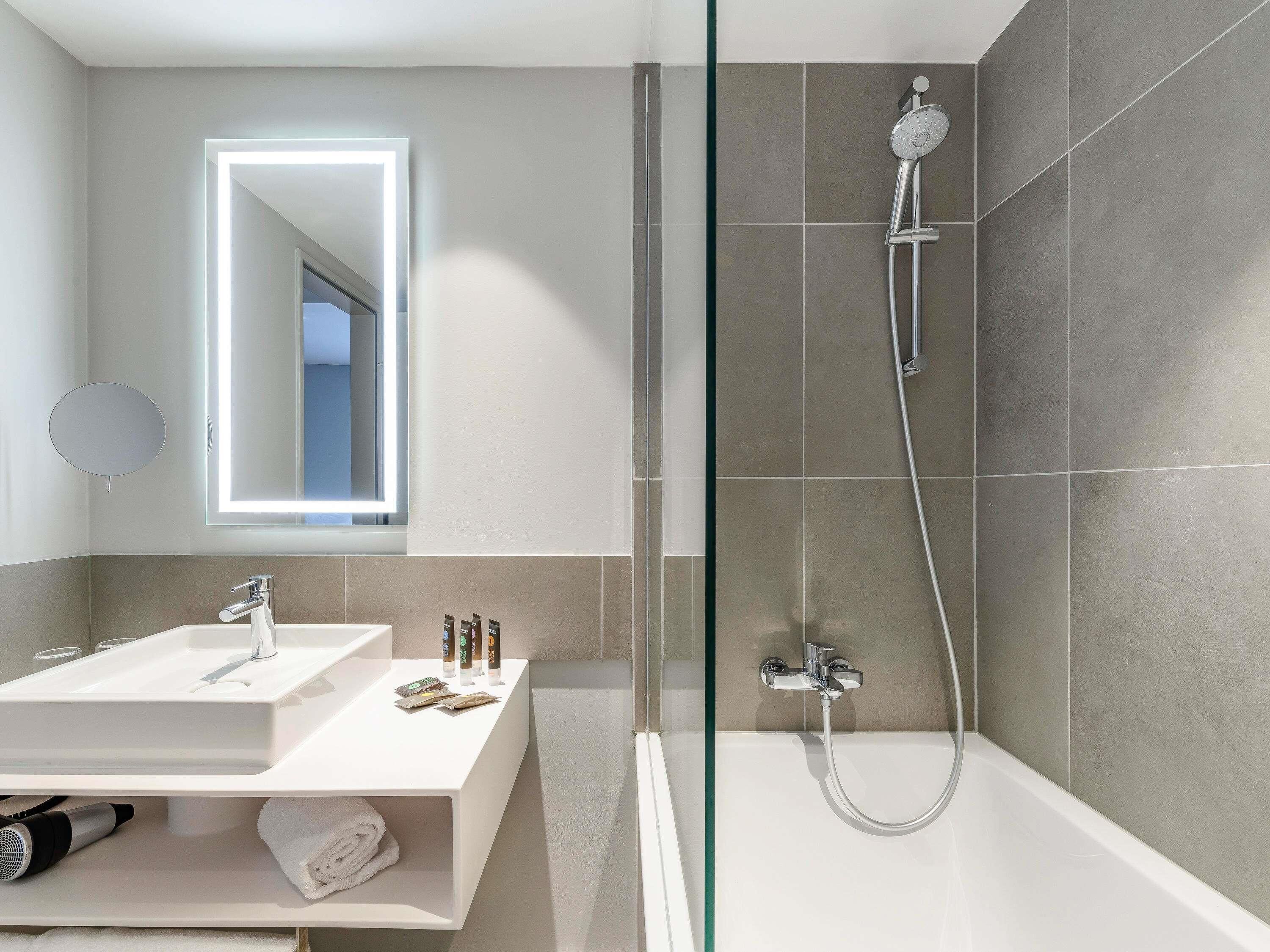 A modern bathroom with a glass shower enclosure, a vanity with two sinks, and a mirror with integrated lighting.