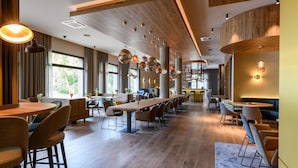 Un comedor moderno con mesas largas y sillas, suelo de madera e iluminación colgante.