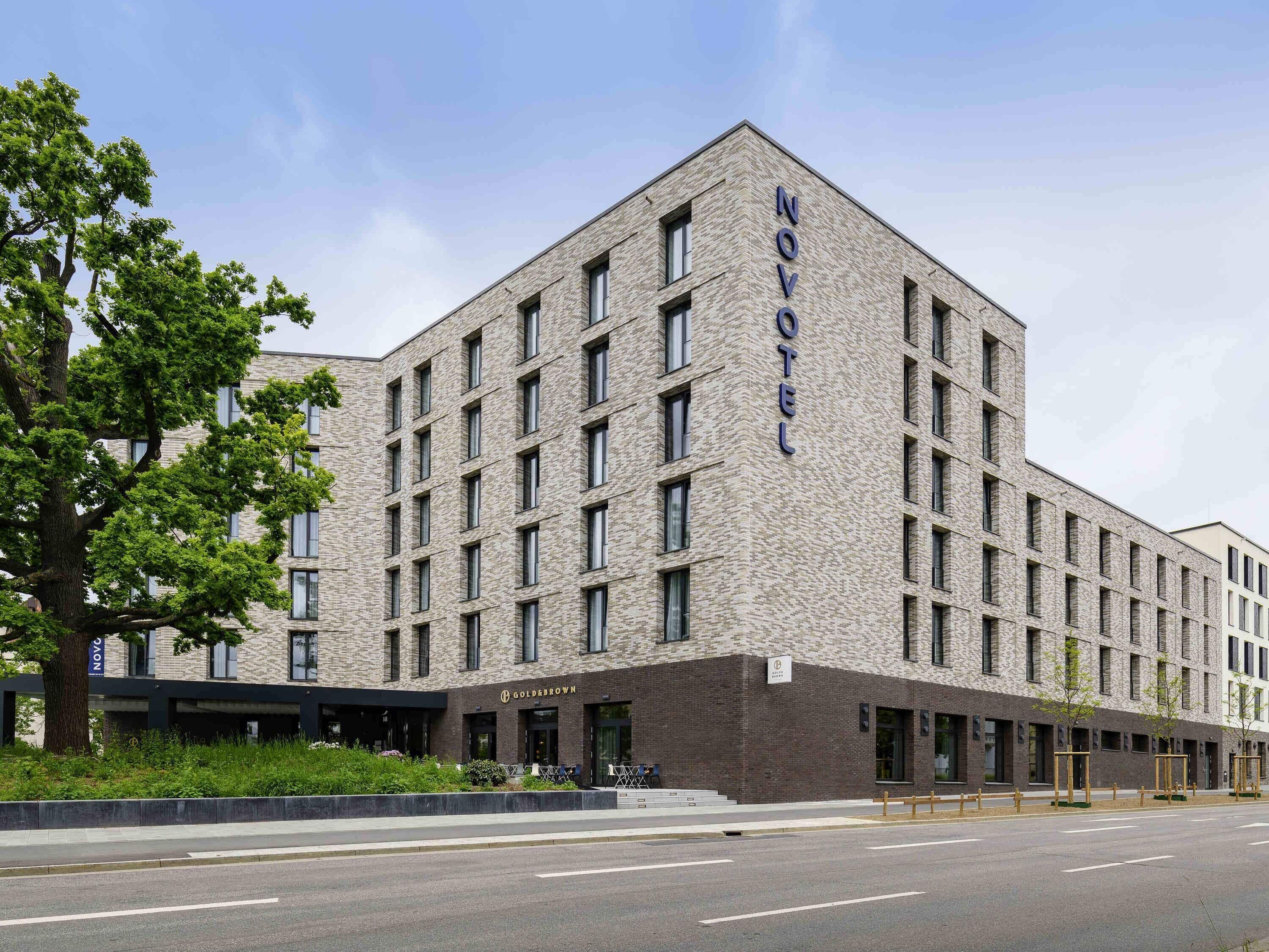 A modern hotel building with a prominent 'NOVOTEL' sign, a brick facade, and a series of windows.