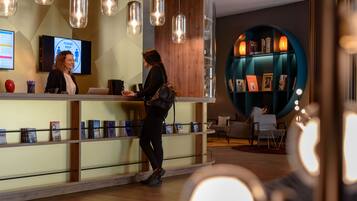 Zona de recepción con un mostrador de madera, una pantalla de televisión y una estantería con revistas.