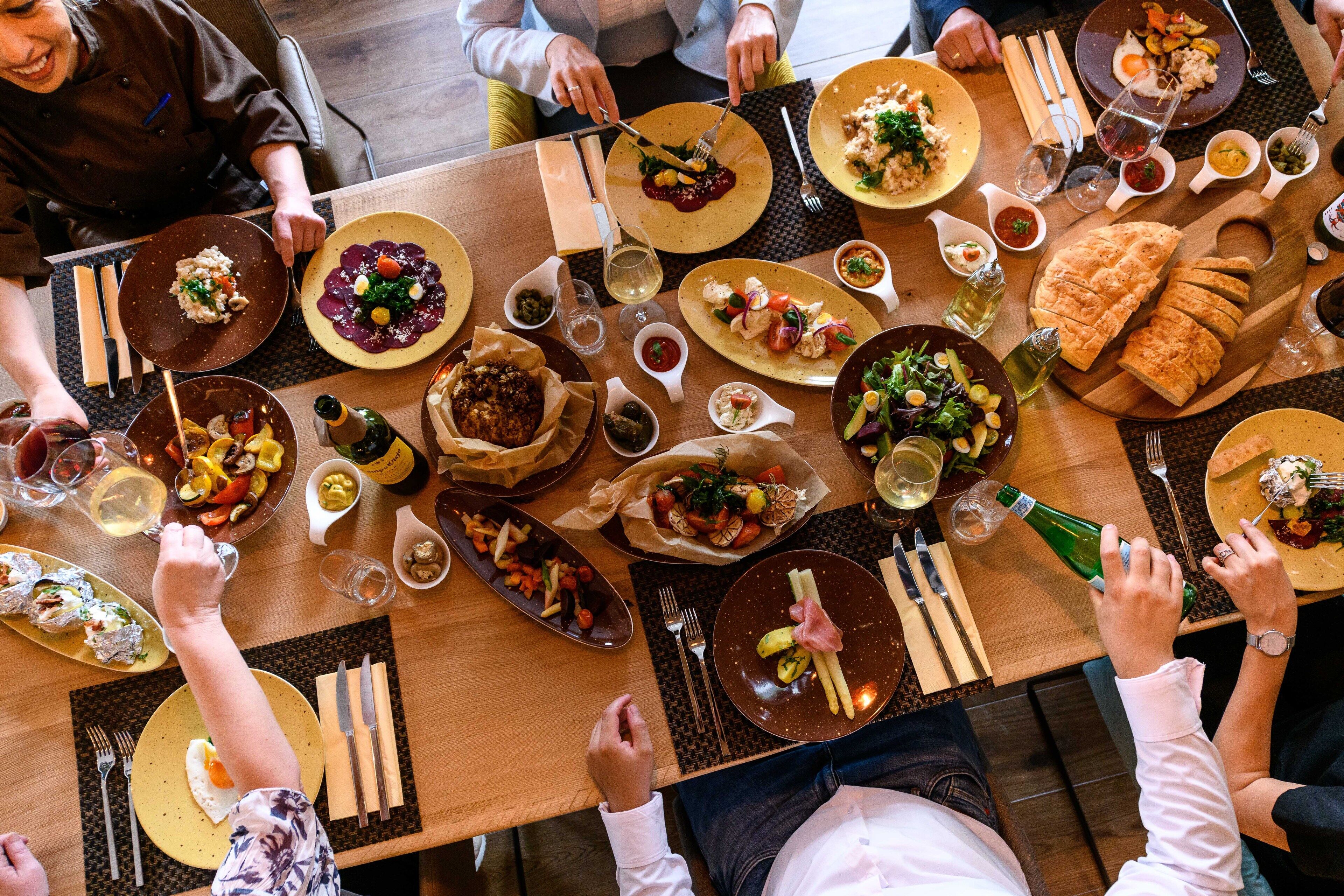 Un groupe de personnes est assis à une table, devant divers plats, des verres de vin et des couverts.