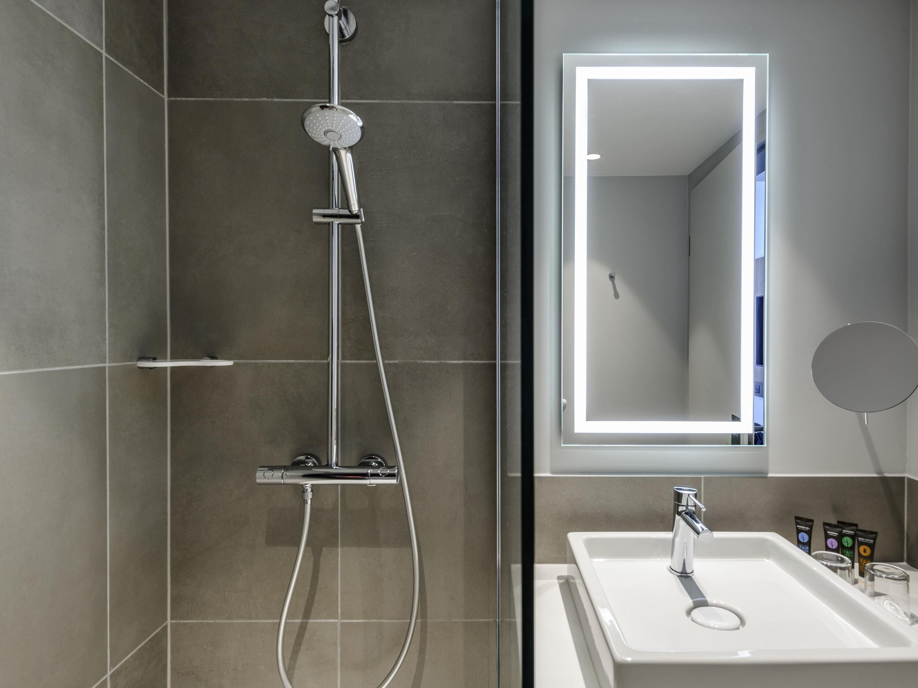 Een moderne badkamer met douche, spiegel en wastafel.