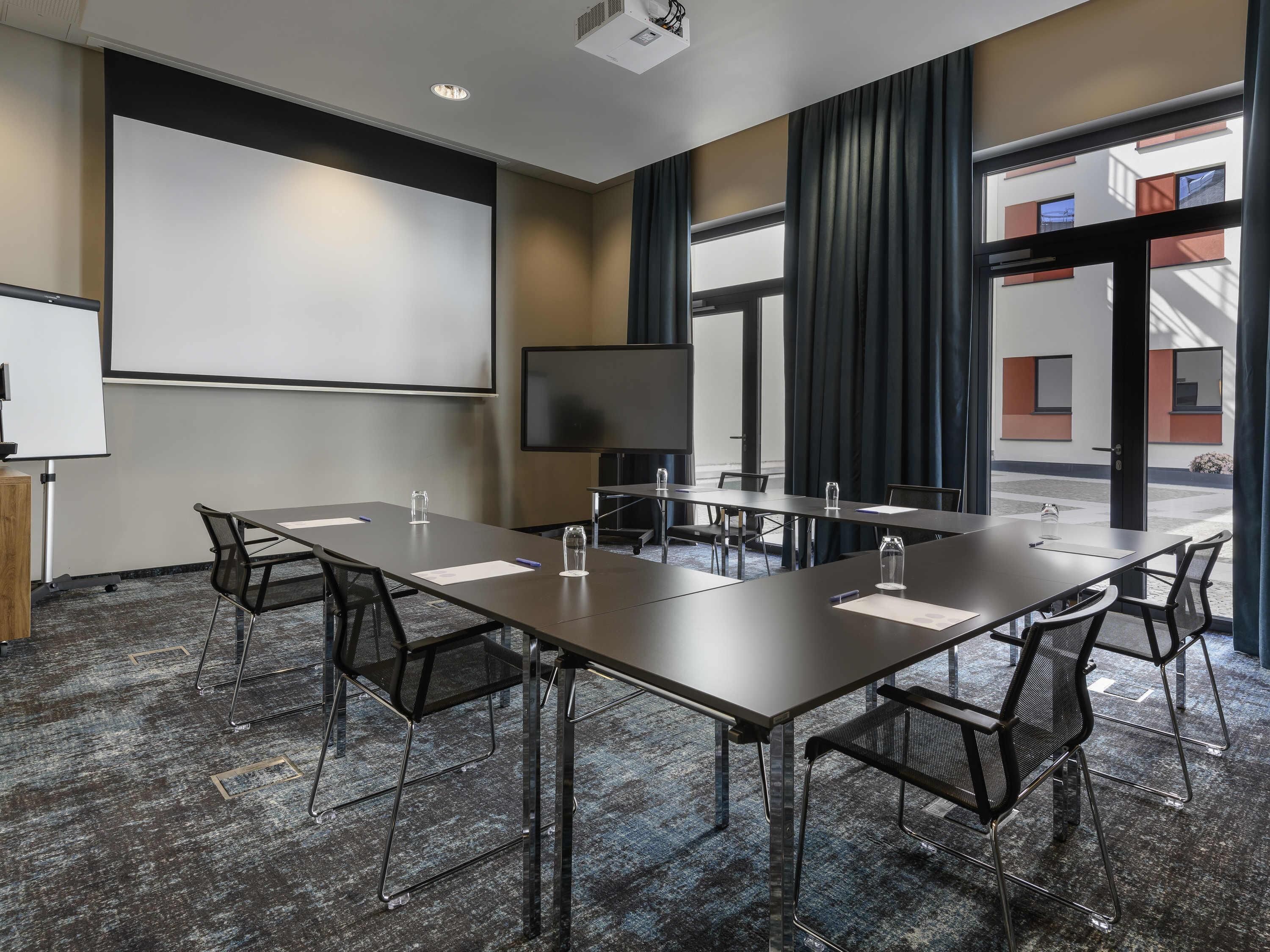 Un salón de conferencias con una larga mesa, sillas, una pantalla de proyector y un televisor.
